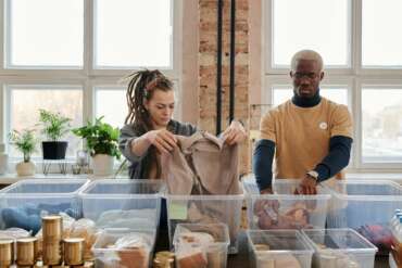 woman with dreadlocks and man in yellow t shirt sorting clothes standing next to each other